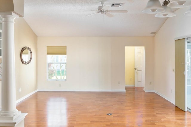 empty room featuring vaulted ceiling, ceiling fan, light wood-type flooring, a textured ceiling, and ornate columns