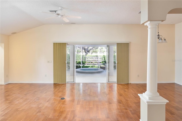 empty room featuring decorative columns, a textured ceiling, ceiling fan with notable chandelier, vaulted ceiling, and hardwood / wood-style flooring