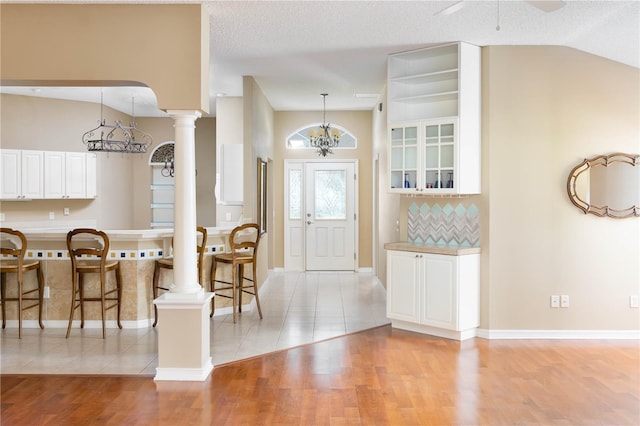 entrance foyer with ornate columns, ceiling fan with notable chandelier, a textured ceiling, vaulted ceiling, and light hardwood / wood-style floors