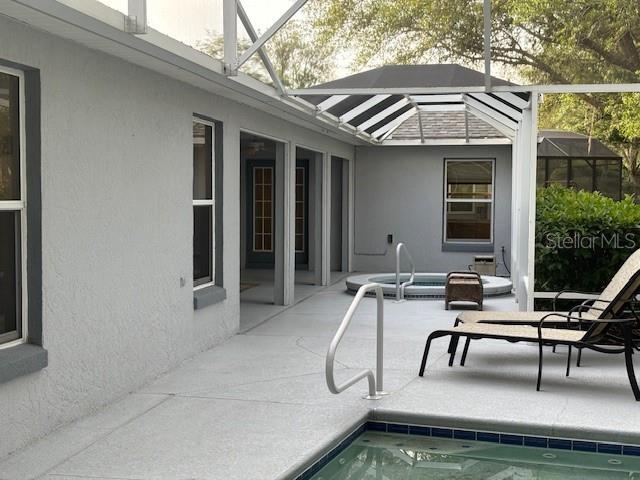 view of swimming pool with an in ground hot tub, glass enclosure, and a patio area