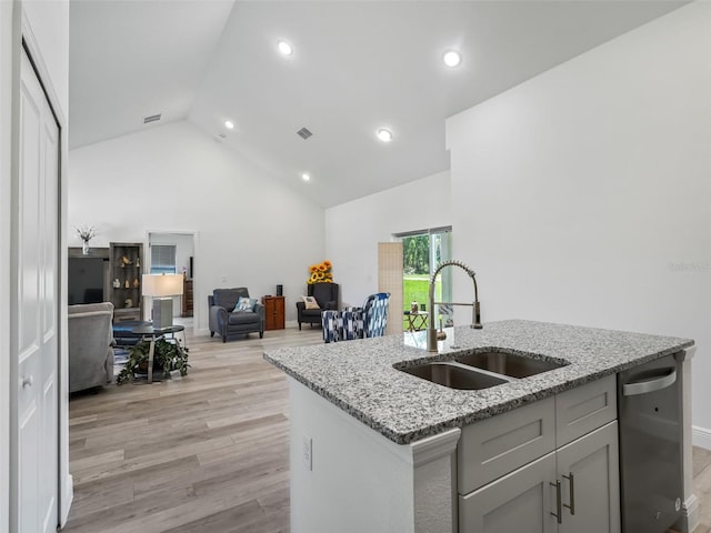 kitchen with light stone countertops, sink, light wood-type flooring, a center island with sink, and dishwasher