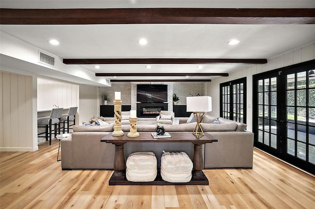 living room with light wood-type flooring, beam ceiling, and a fireplace