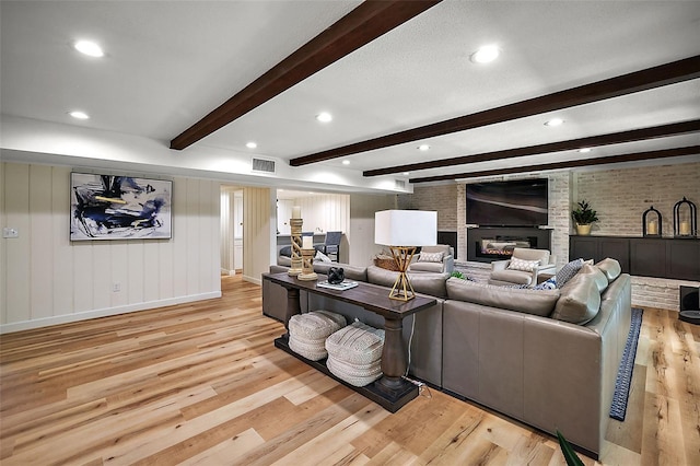 living room featuring brick wall, light hardwood / wood-style floors, beamed ceiling, and a fireplace