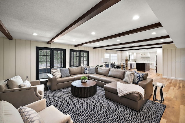 living room with beamed ceiling, light hardwood / wood-style flooring, french doors, and a textured ceiling