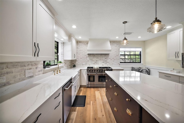 kitchen featuring decorative light fixtures, appliances with stainless steel finishes, custom exhaust hood, white cabinetry, and light wood-type flooring