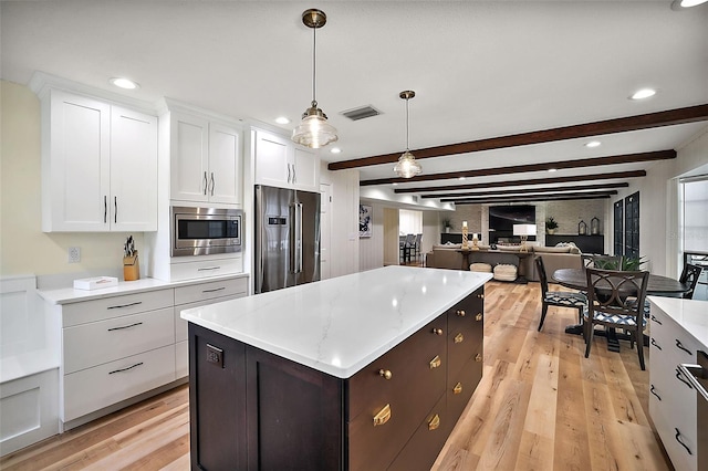 kitchen with decorative light fixtures, a kitchen island, stainless steel appliances, beam ceiling, and light wood-type flooring