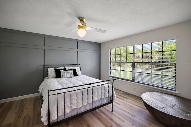 bedroom featuring light hardwood / wood-style flooring, ceiling fan, a textured ceiling, and multiple windows