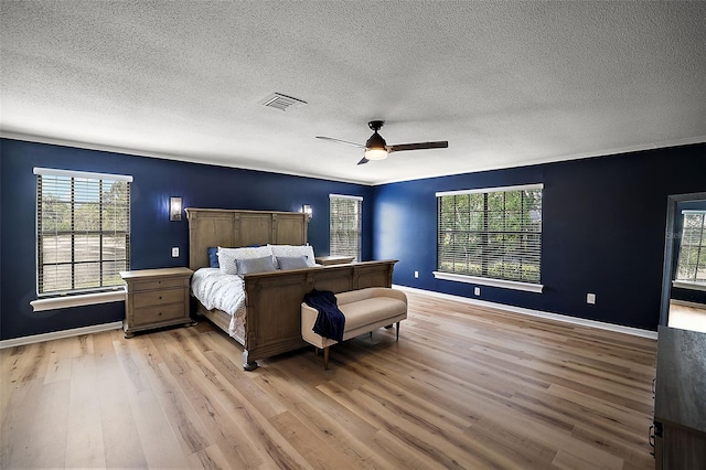 bedroom with light hardwood / wood-style flooring, ceiling fan, multiple windows, and a textured ceiling