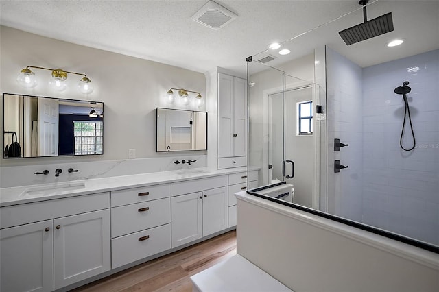 bathroom featuring double sink vanity, hardwood / wood-style flooring, a shower with shower door, and a textured ceiling