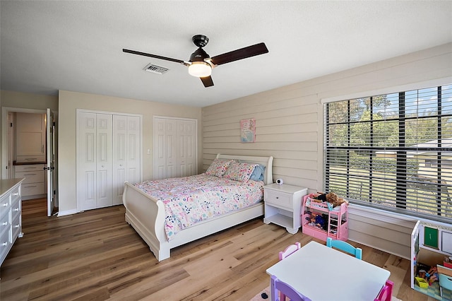 bedroom featuring wood-type flooring, ceiling fan, and multiple closets