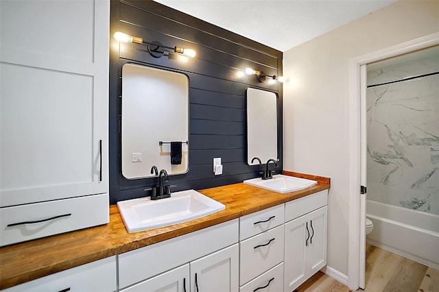 full bathroom featuring wood-type flooring, tiled shower / bath combo, toilet, and dual bowl vanity