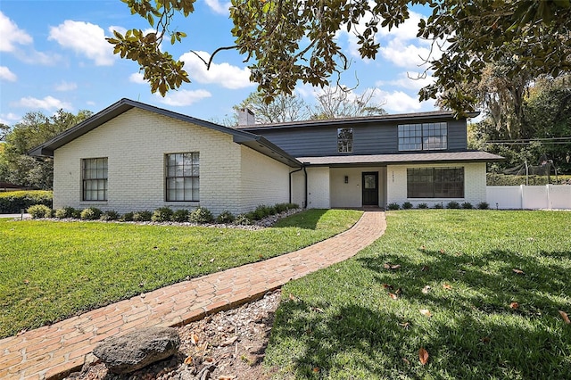 view of front facade featuring a front yard, brick siding, a chimney, and fence