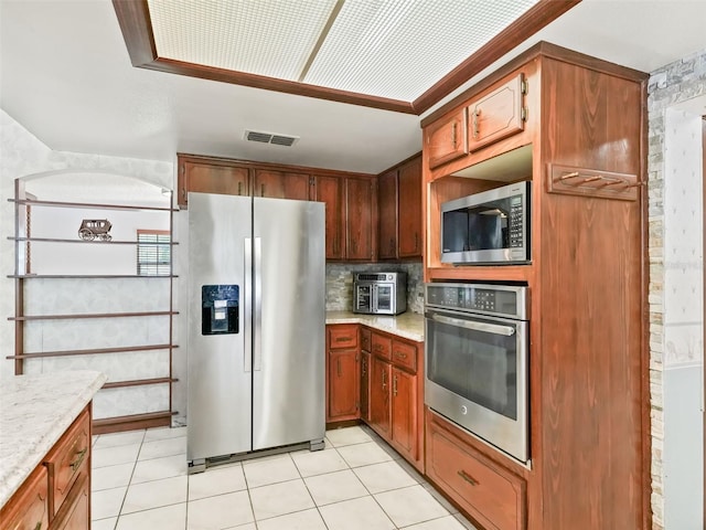 kitchen featuring backsplash, light stone countertops, stainless steel appliances, and light tile floors