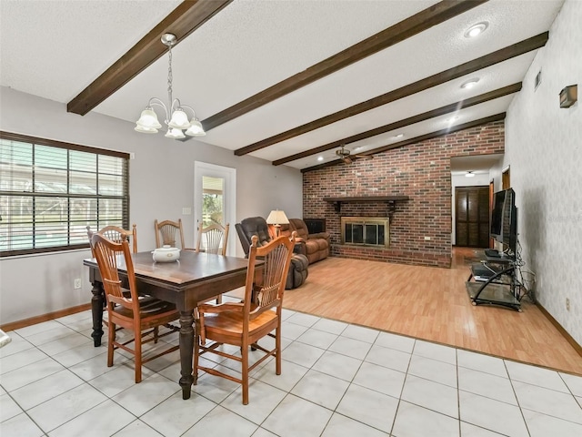 dining space with brick wall, a brick fireplace, light hardwood / wood-style flooring, ceiling fan with notable chandelier, and vaulted ceiling with beams