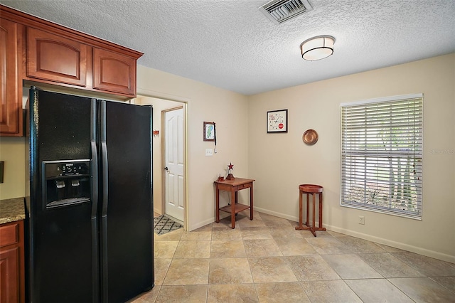 kitchen featuring light stone countertops, black fridge, a textured ceiling, and light tile floors