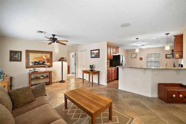 living room with tile flooring, ceiling fan, and a textured ceiling