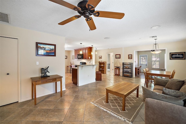 living room with tile flooring, ceiling fan, and a textured ceiling