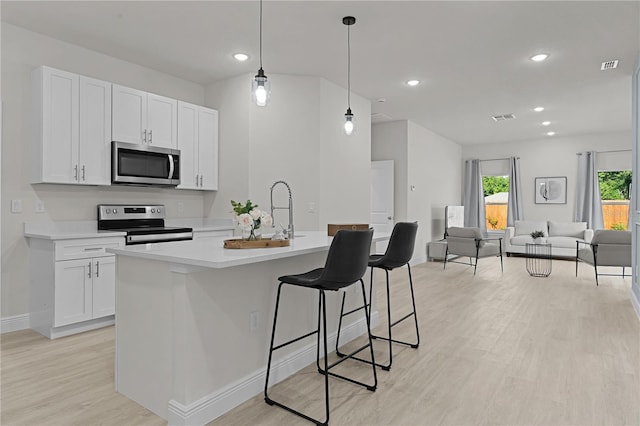 kitchen with white cabinetry, stainless steel appliances, hanging light fixtures, light hardwood / wood-style flooring, and a kitchen island with sink