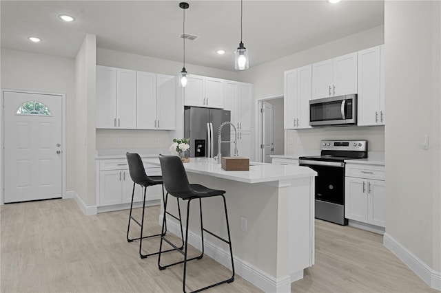 kitchen with a breakfast bar area, light hardwood / wood-style flooring, white cabinets, stainless steel appliances, and pendant lighting