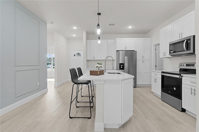 kitchen with white cabinetry, an island with sink, light wood-type flooring, sink, and appliances with stainless steel finishes