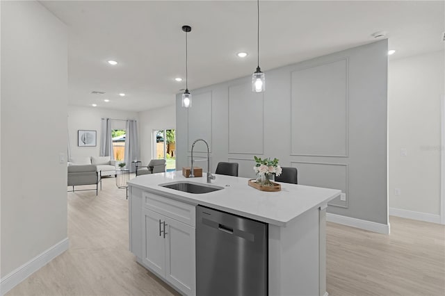 kitchen with light hardwood / wood-style flooring, a kitchen island with sink, stainless steel dishwasher, pendant lighting, and sink