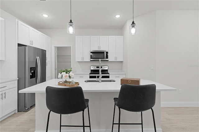 kitchen featuring stainless steel appliances, sink, light wood-type flooring, and an island with sink