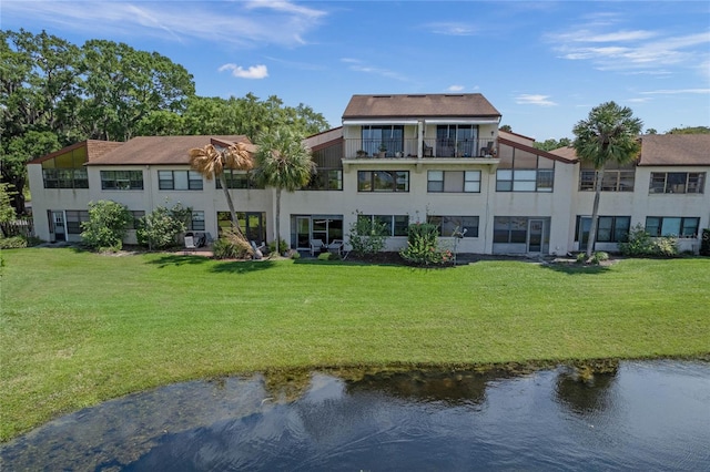 rear view of property featuring a balcony, a water view, and a lawn