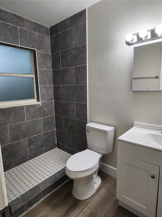 bathroom featuring toilet, hardwood / wood-style floors, vanity, and tiled shower