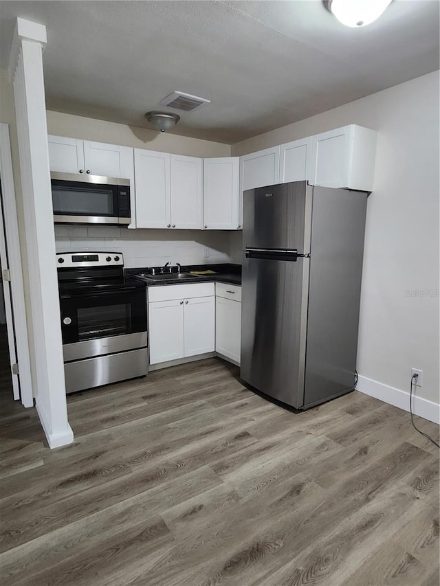 kitchen with stainless steel appliances, white cabinetry, and hardwood / wood-style flooring