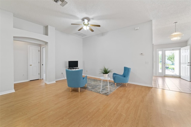 unfurnished room featuring ceiling fan with notable chandelier, a textured ceiling, and light wood-type flooring