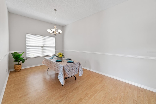 dining area with light hardwood / wood-style flooring, a textured ceiling, and a notable chandelier