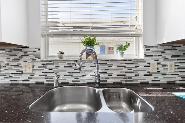 interior details featuring white cabinets, decorative backsplash, dark stone countertops, and sink