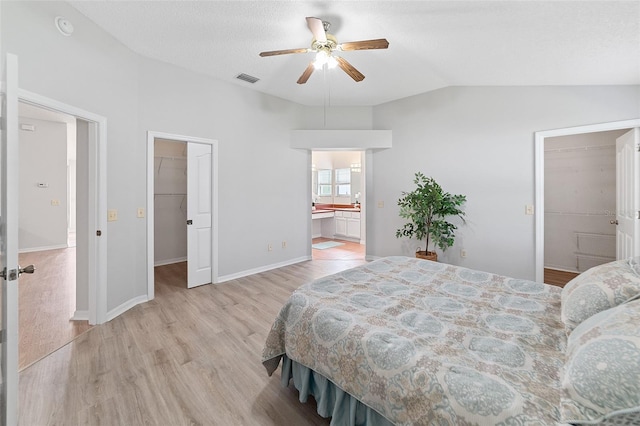 bedroom with ensuite bath, ceiling fan, light hardwood / wood-style flooring, vaulted ceiling, and a walk in closet