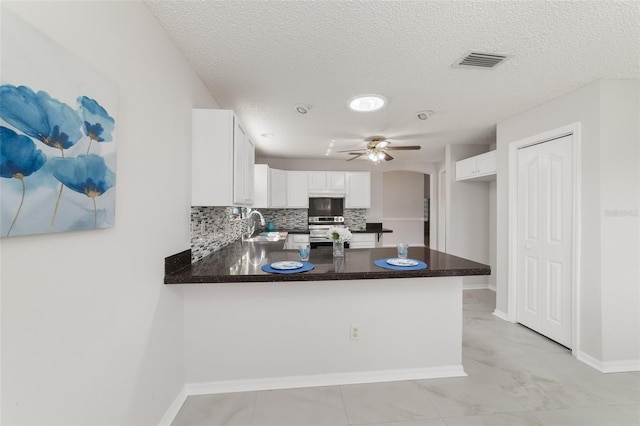 kitchen with kitchen peninsula, white cabinets, ceiling fan, and stainless steel range oven