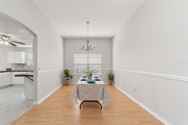 dining space with ceiling fan with notable chandelier, light hardwood / wood-style floors, and a textured ceiling