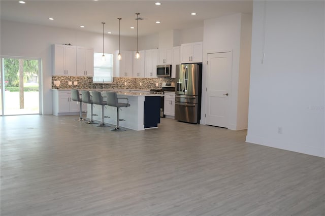 kitchen featuring hanging light fixtures, stainless steel appliances, white cabinets, a center island, and a breakfast bar area