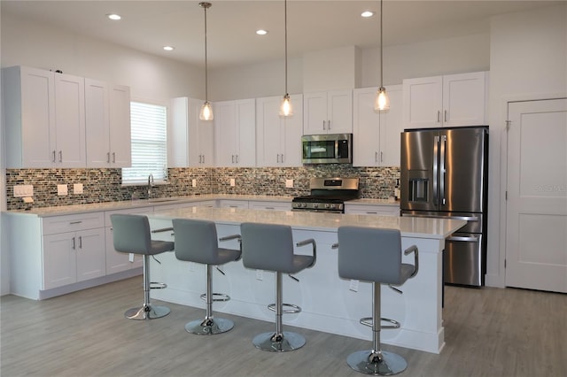 kitchen featuring pendant lighting, a kitchen breakfast bar, a kitchen island, appliances with stainless steel finishes, and light wood-type flooring