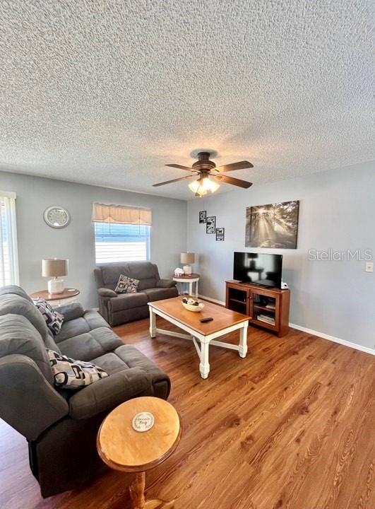 living room with a textured ceiling, wood-type flooring, and ceiling fan