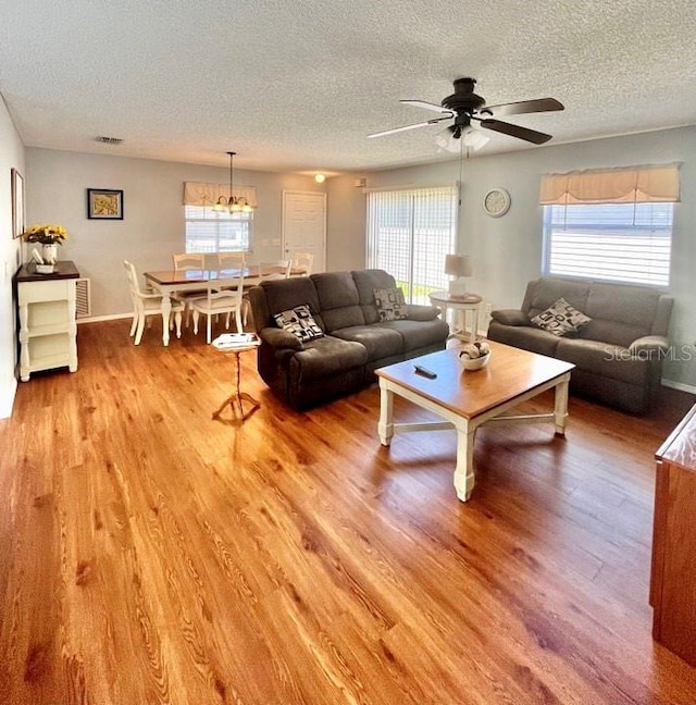 living room featuring light hardwood / wood-style floors, a textured ceiling, and ceiling fan with notable chandelier