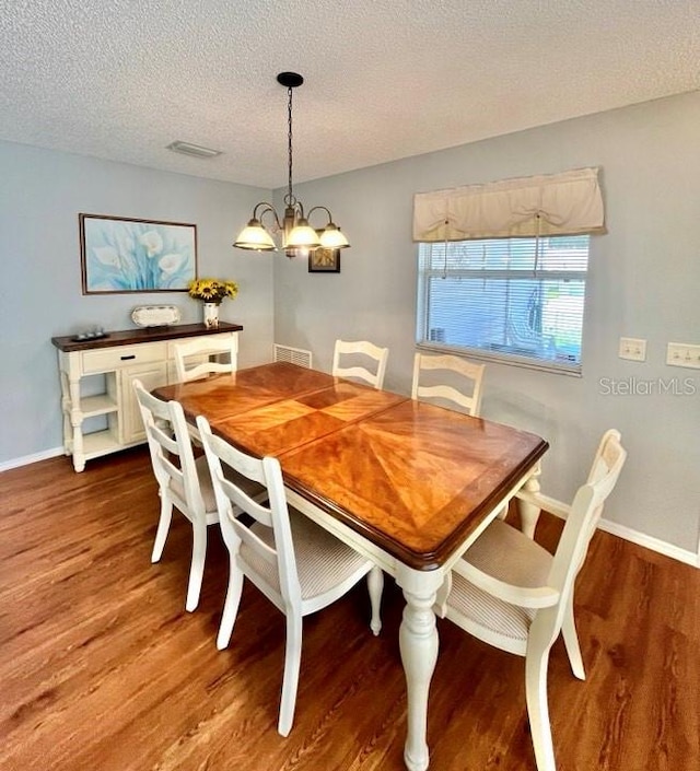 dining area with dark hardwood / wood-style flooring, an inviting chandelier, and a textured ceiling