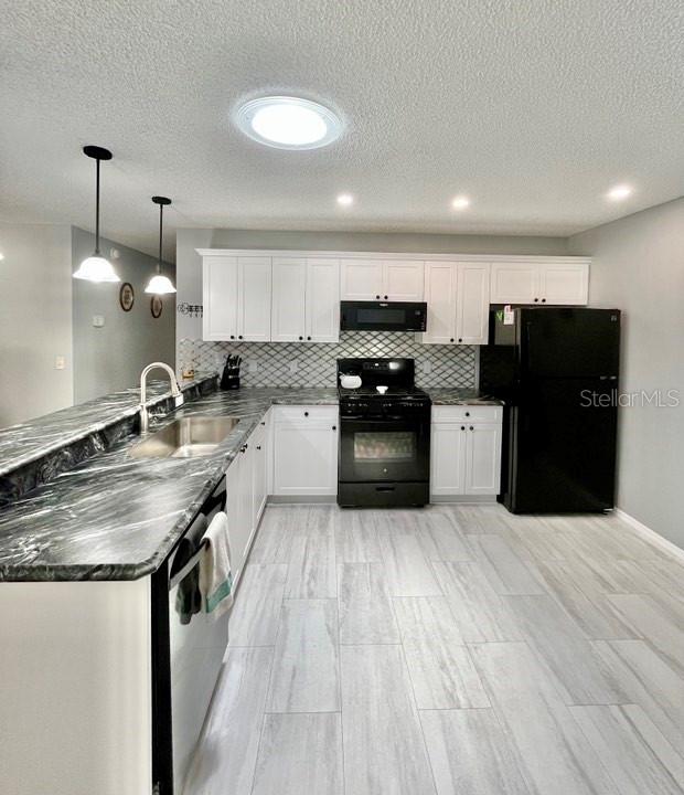 kitchen with kitchen peninsula, sink, hanging light fixtures, white cabinets, and black appliances