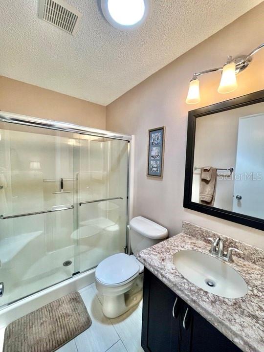 bathroom featuring tile floors, a textured ceiling, toilet, vanity, and an enclosed shower