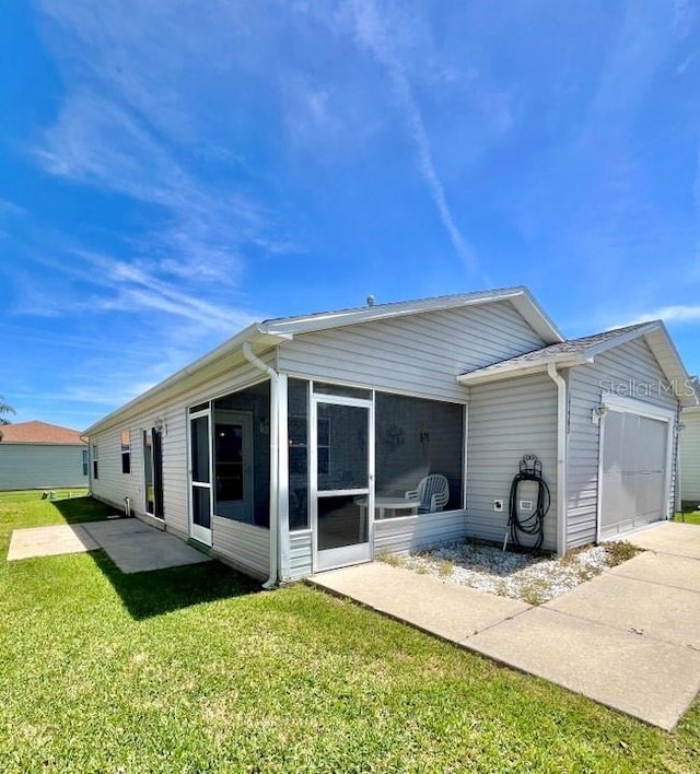 back of house featuring a sunroom, a lawn, and a garage