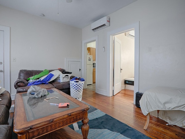 bedroom featuring an AC wall unit, ensuite bathroom, light hardwood / wood-style flooring, and white refrigerator