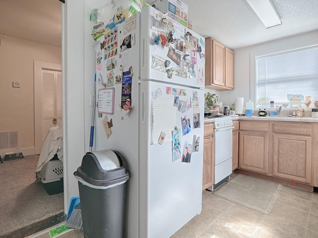 kitchen with light brown cabinetry, white appliances, a textured ceiling, and light tile floors