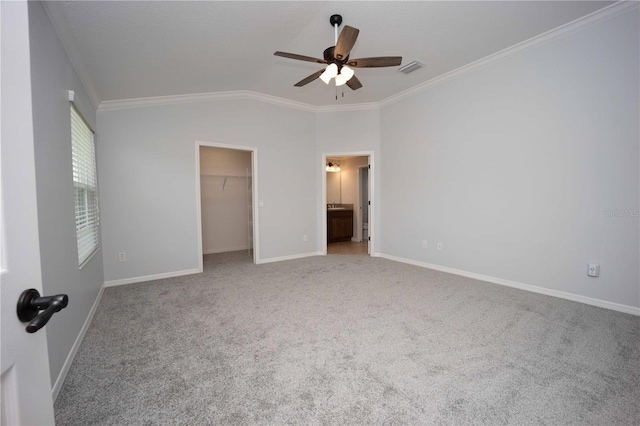 unfurnished bedroom with light colored carpet, crown molding, ceiling fan, lofted ceiling, and a walk in closet