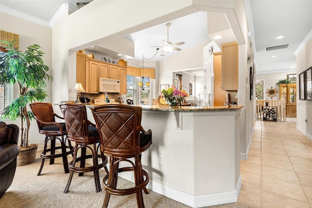 kitchen featuring stone countertops, a kitchen breakfast bar, ceiling fan, crown molding, and light tile floors