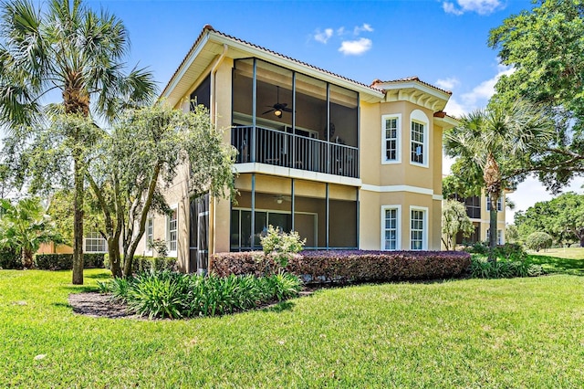 back of property featuring ceiling fan, a lawn, and a balcony