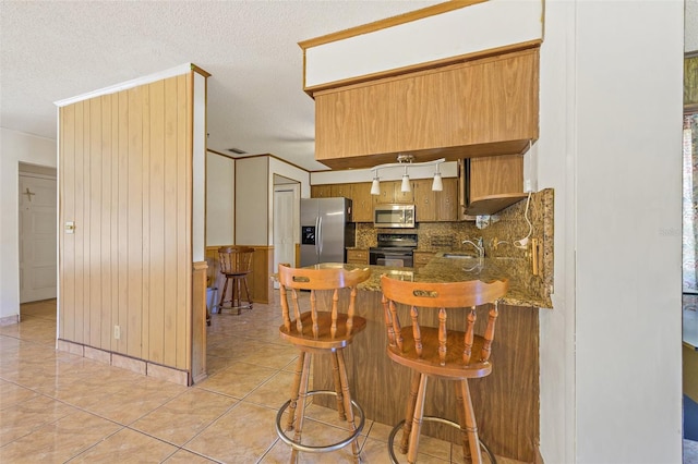 kitchen featuring backsplash, kitchen peninsula, appliances with stainless steel finishes, light tile floors, and a kitchen bar