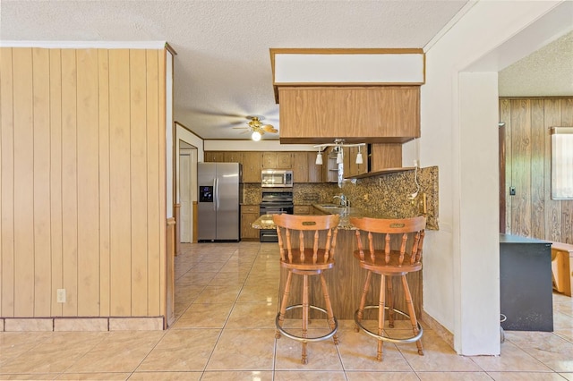 kitchen featuring ceiling fan, range, fridge, light tile flooring, and kitchen peninsula